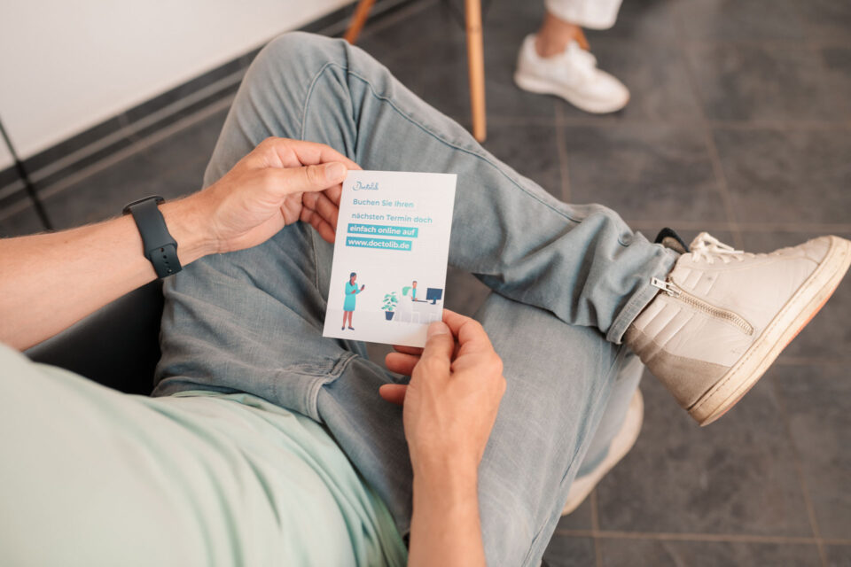 Patient hält Doctolib Flyer zur Terminvereinbarung in der Hand